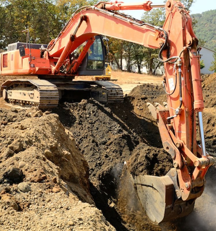 Large track hoe excavator digging out old rock and soil during preperation at a new commercial development road construction project